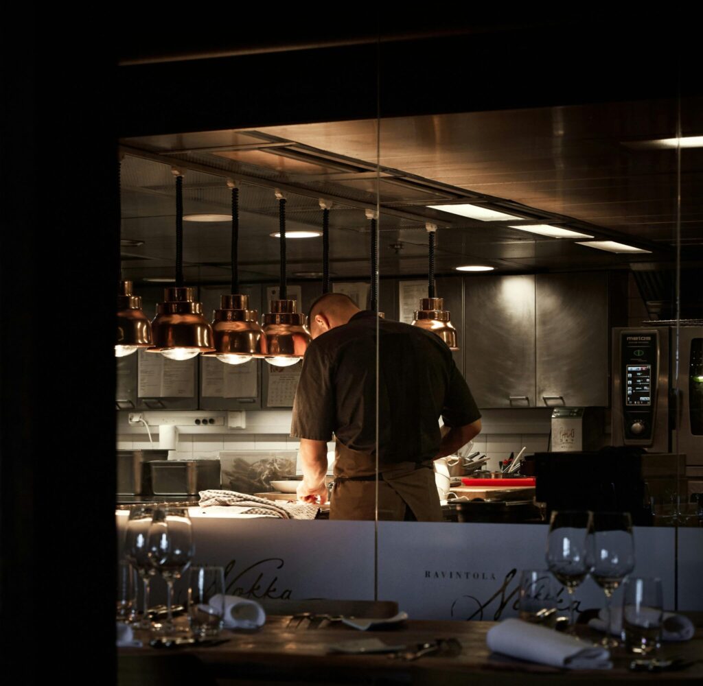 A chef preparing dishes in a stylish restaurant kitchen with dim lighting.